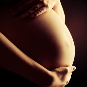 Close-up of a pregnant woman's tummy. Over black background